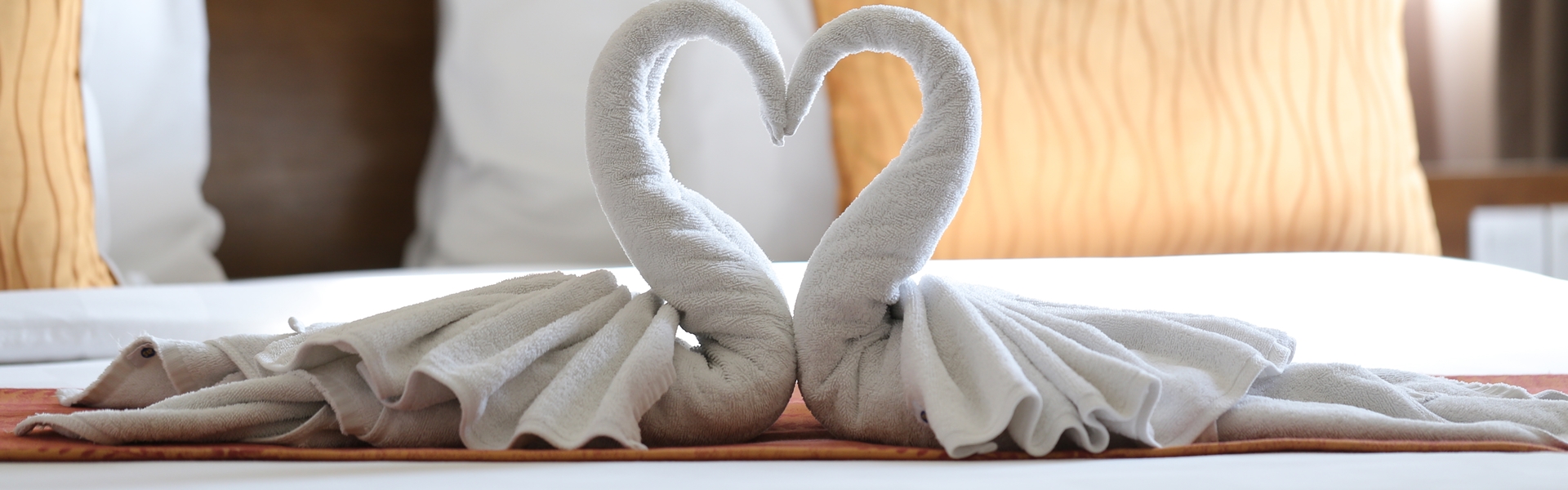 Two Swans Made Of Towels Forming Heart Shape On Bed In Honeymoon